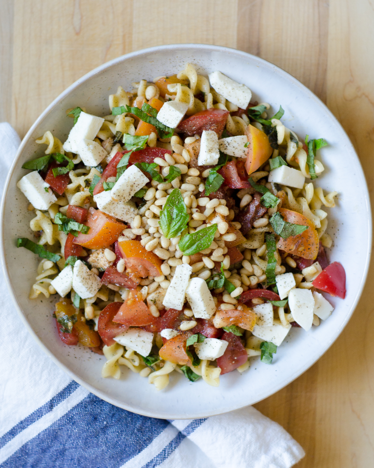 A quick and delicious recipe for caprese pasta with tomatoes, fresh mozzarella, basil, and pine nuts. A crowd pleaser that's ready in under 30 minutes!