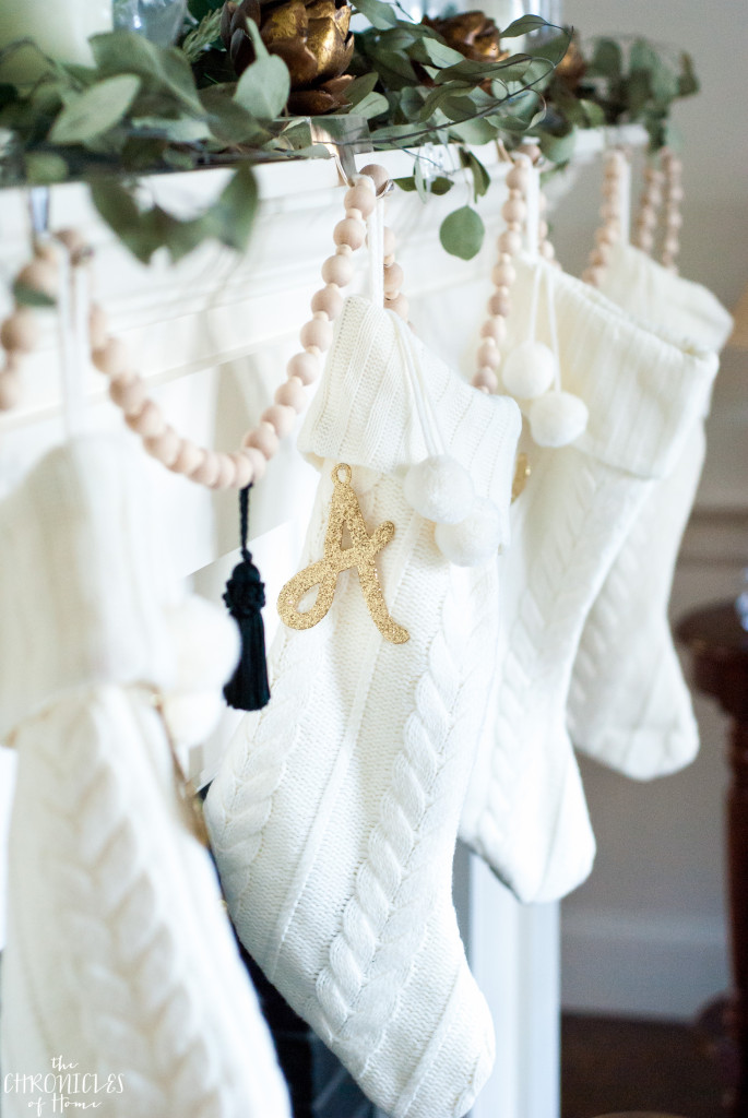 Classic cable knit stockings hung with a DIY wood bead garland, black tassels, and glittered monogram letters