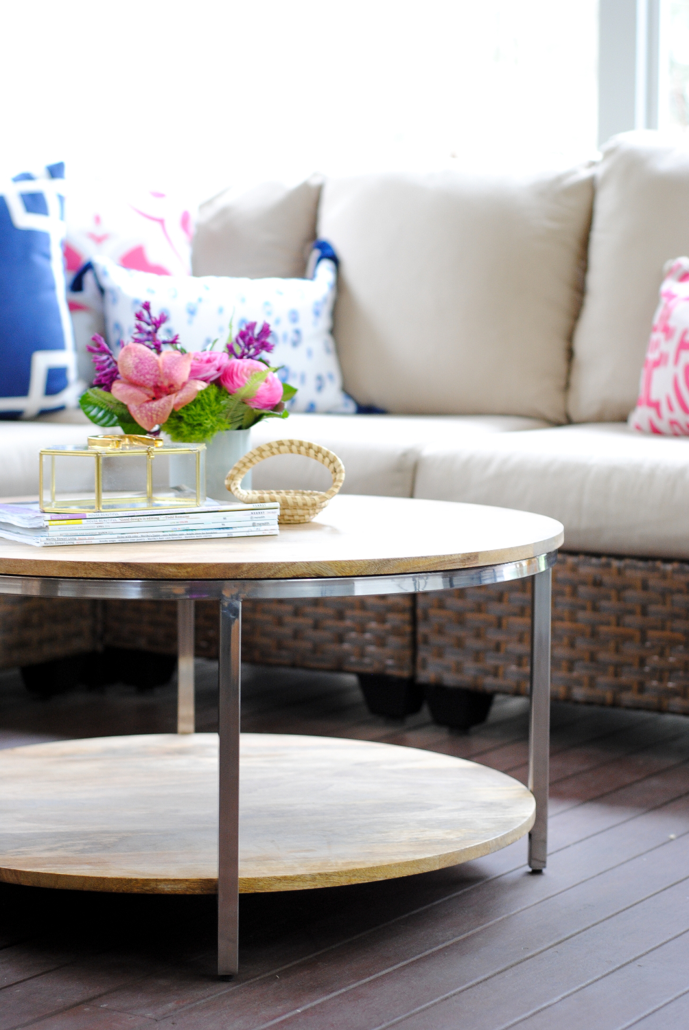 Screened porch with woven wicker, round coffee table, navy blue and pink accents - classic with a touch of contemporary!