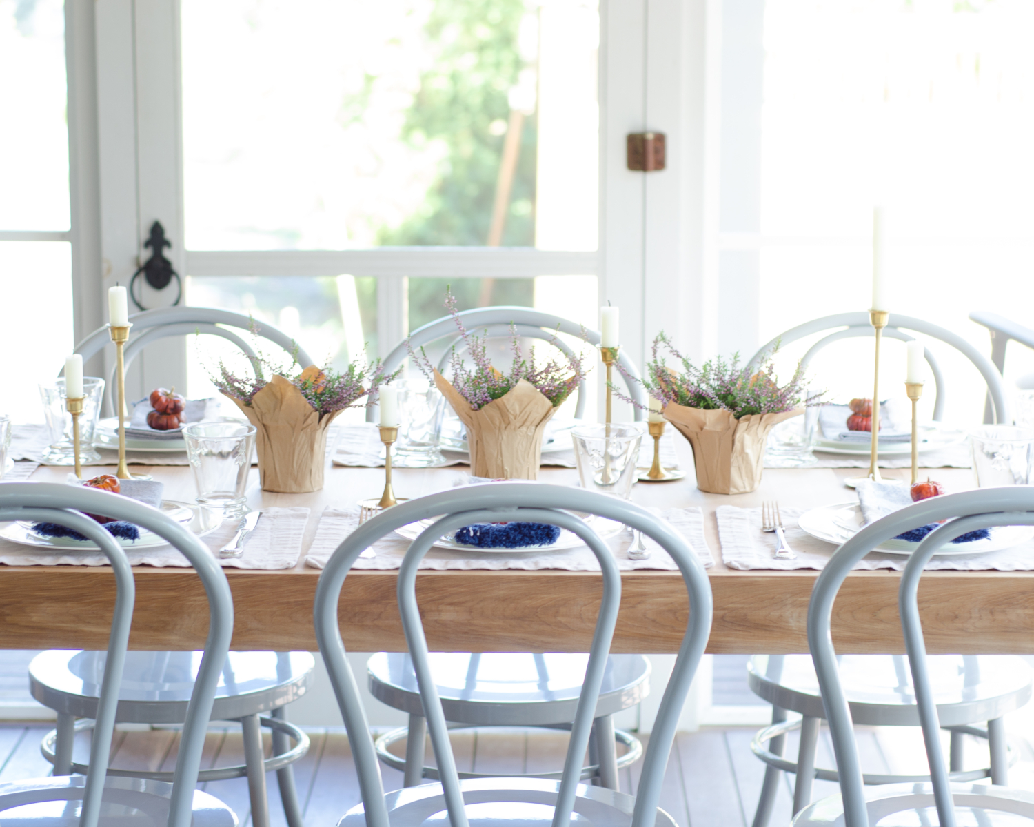 Fall outdoor dinner party with a simple table with mini pumpkins, brass candlesticks, and miniature flower pots. Metal bentwood chairs are perfect for light outdoor use!