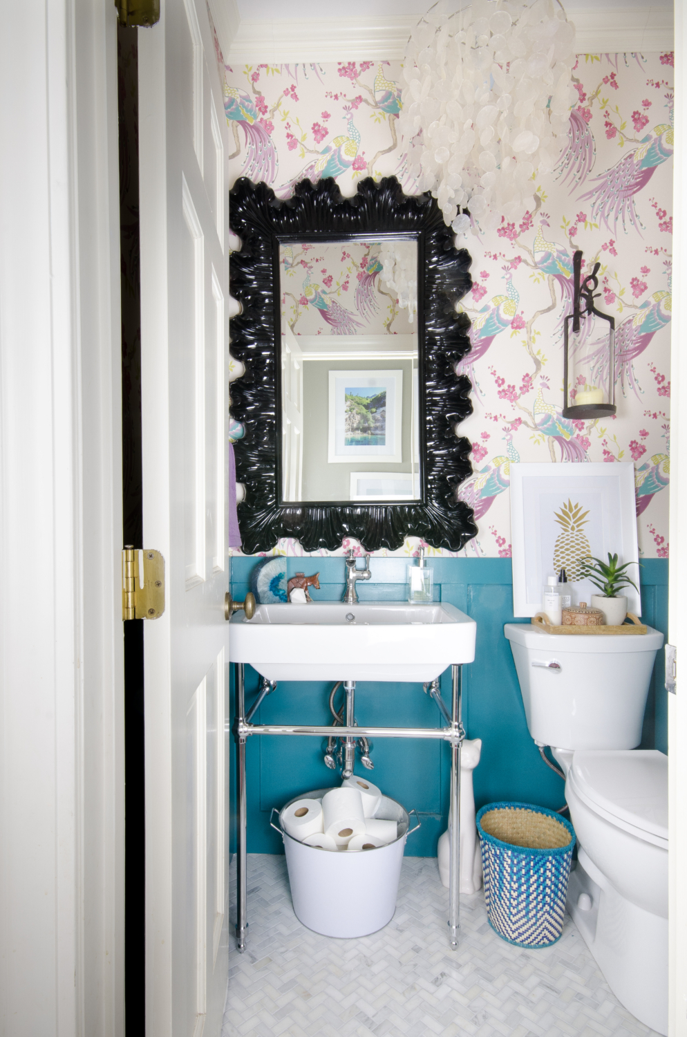 A small powder room gets a majorly gorgeous makeover, including marble tile, console sink, bird wallpaper, and capiz shell pendant. You won't believe this before and after!