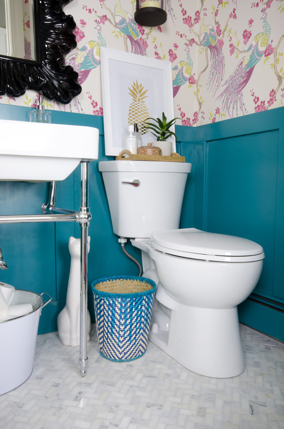 A small powder room gets a majorly gorgeous makeover, including marble tile, teal wainscoting, console sink, bird wallpaper, and capiz shell pendant. You won't believe this before and after!