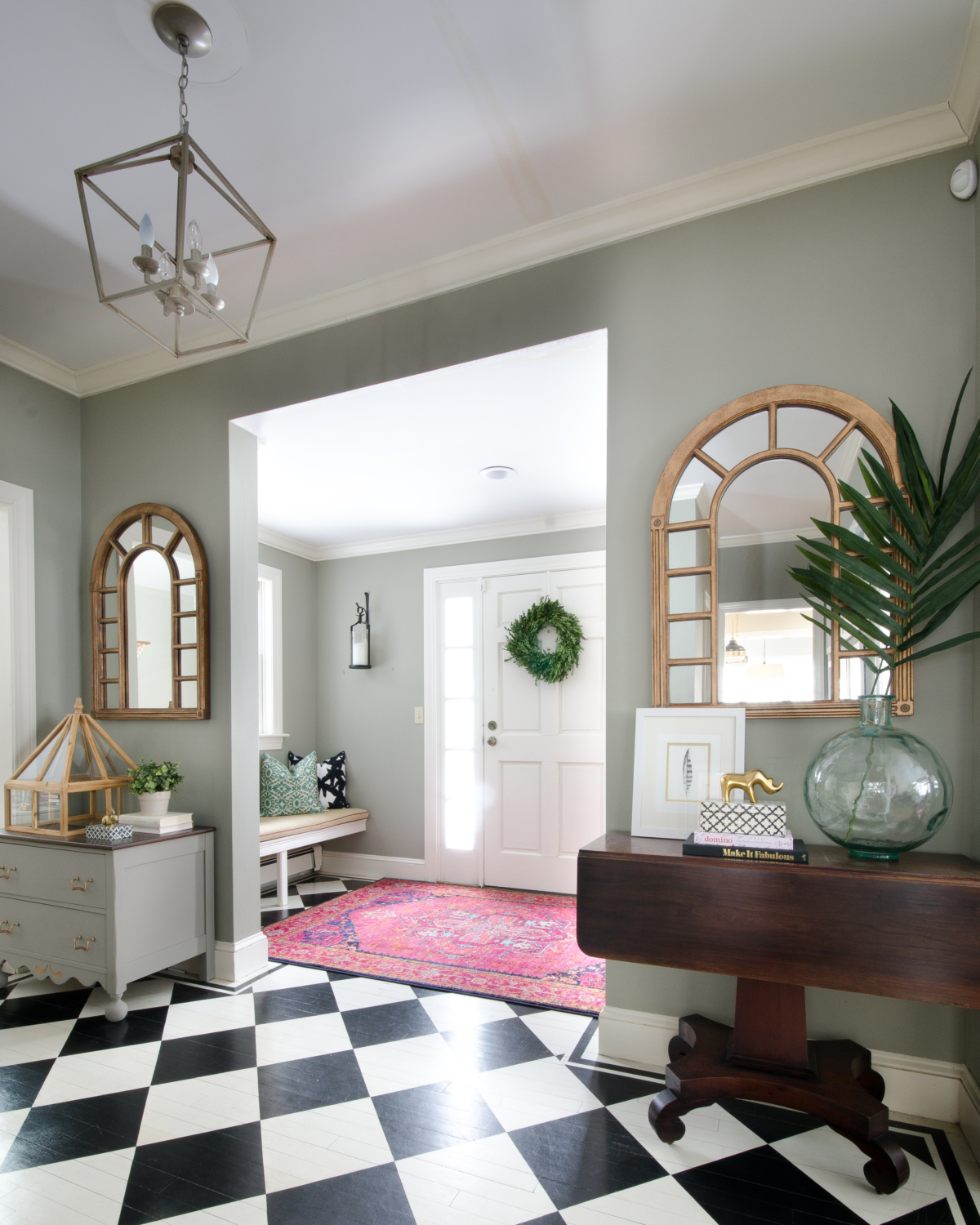 Entryway with built in bench seat, black and white checkered floors, pink rug, gold arched mirrors