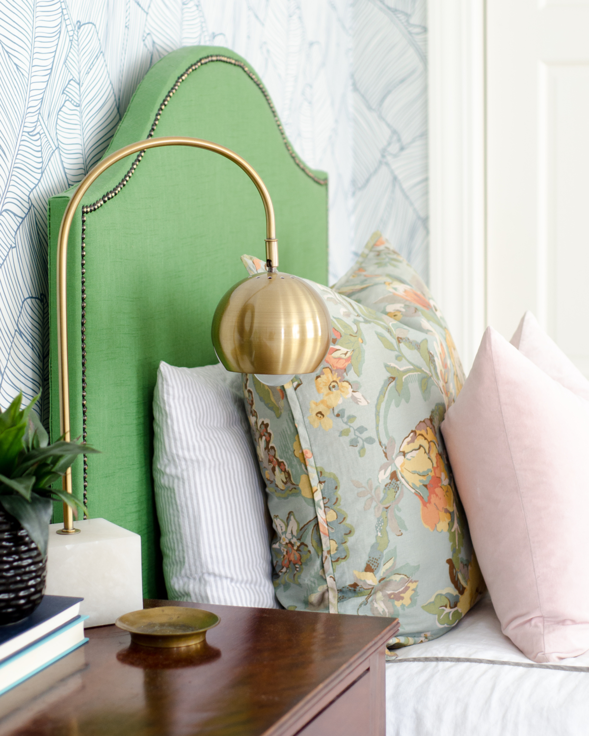 Gorgeous guest room with palm wallpaper, green linen headboards, mustard yellow leather benches, and accents of blush and coral