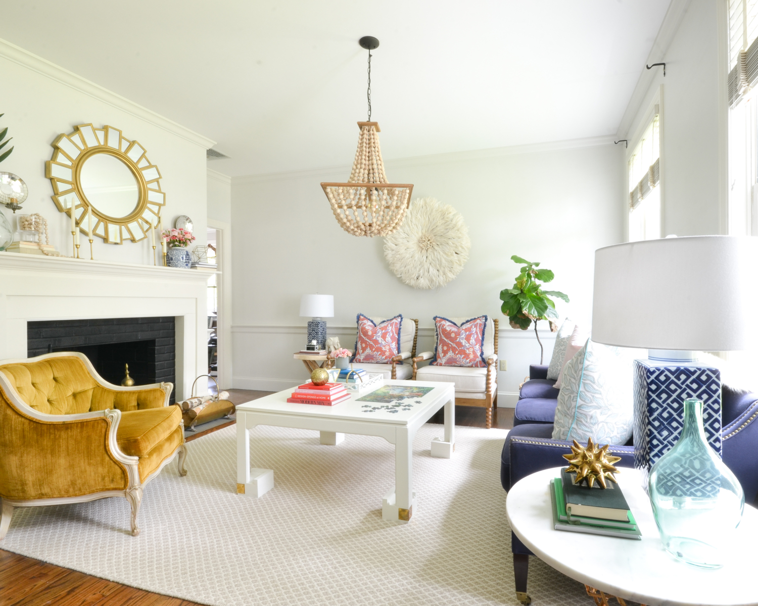 Living room with a neutral base, gold, navy blue, coral. Juju hat feather wall hanging is a striking centerpiece.