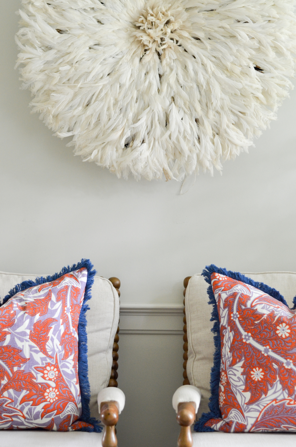 Living room with a neutral base, gold, navy blue, coral. Juju hat feather wall hanging is a striking centerpiece.