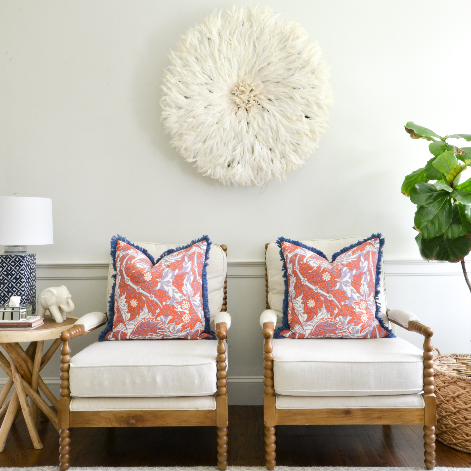 Living room with a neutral base, gold, navy blue, coral. Juju hat feather wall hanging is a striking centerpiece.