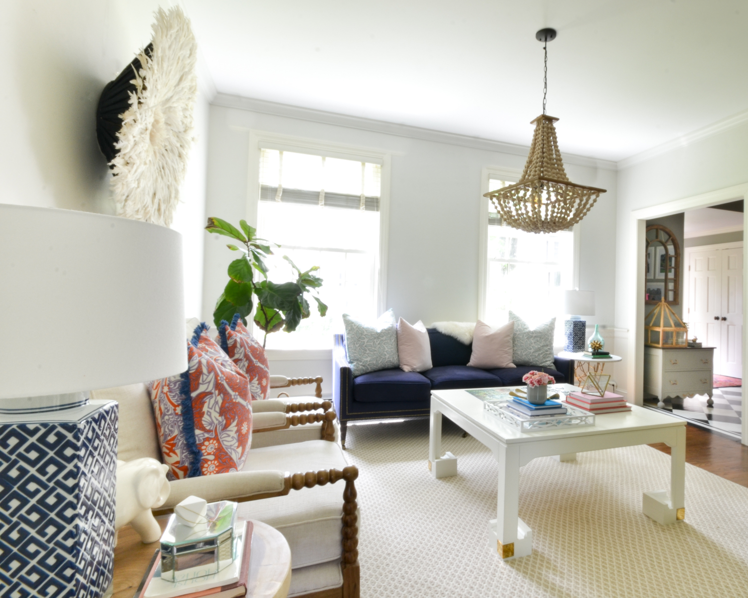 Living room with a neutral base, gold, navy blue, coral. Juju hat feather wall hanging is a striking centerpiece.