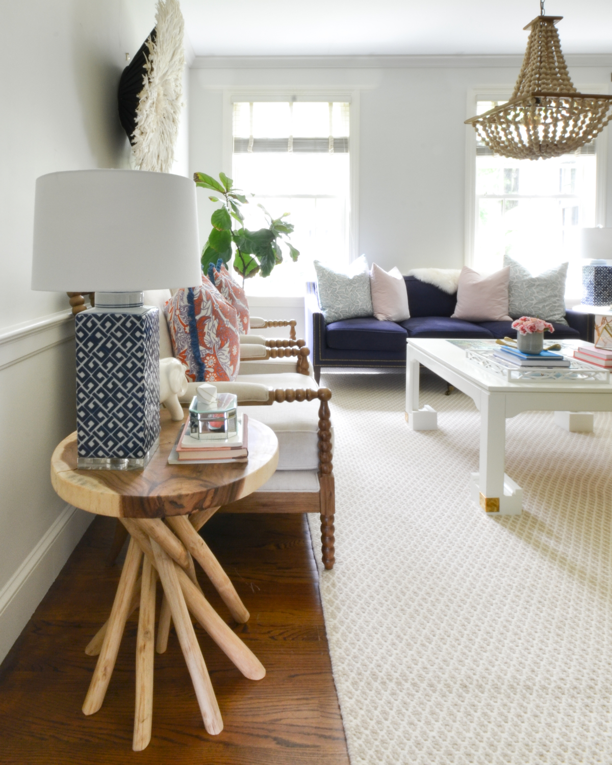 Living room with a neutral base, gold, navy blue, coral. Juju hat feather wall hanging is a striking centerpiece.