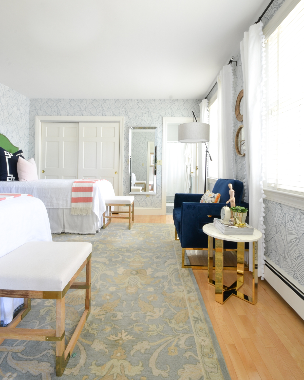 Wallpapered bedroom with twin beds, green upholstered headboards, navy blue, brass, and coral accents