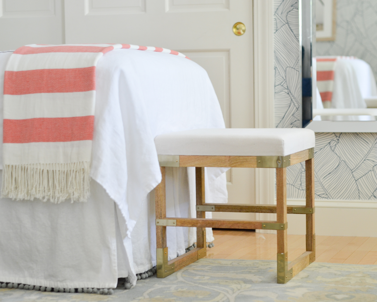 Wallpapered bedroom with twin beds, green upholstered headboards, navy blue, brass, and coral accents