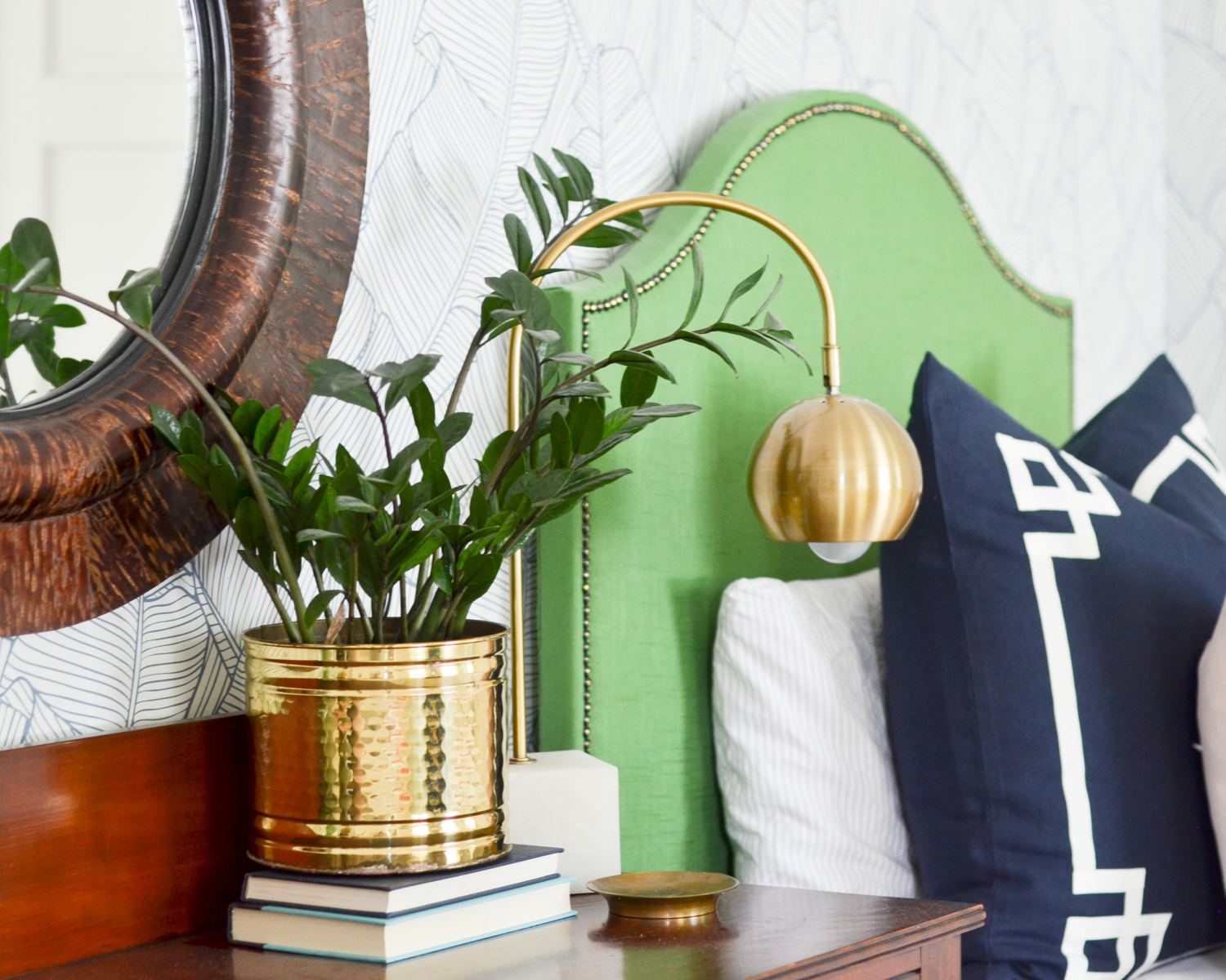 Wallpapered bedroom with twin beds, green upholstered headboards, navy blue, brass, and coral accents