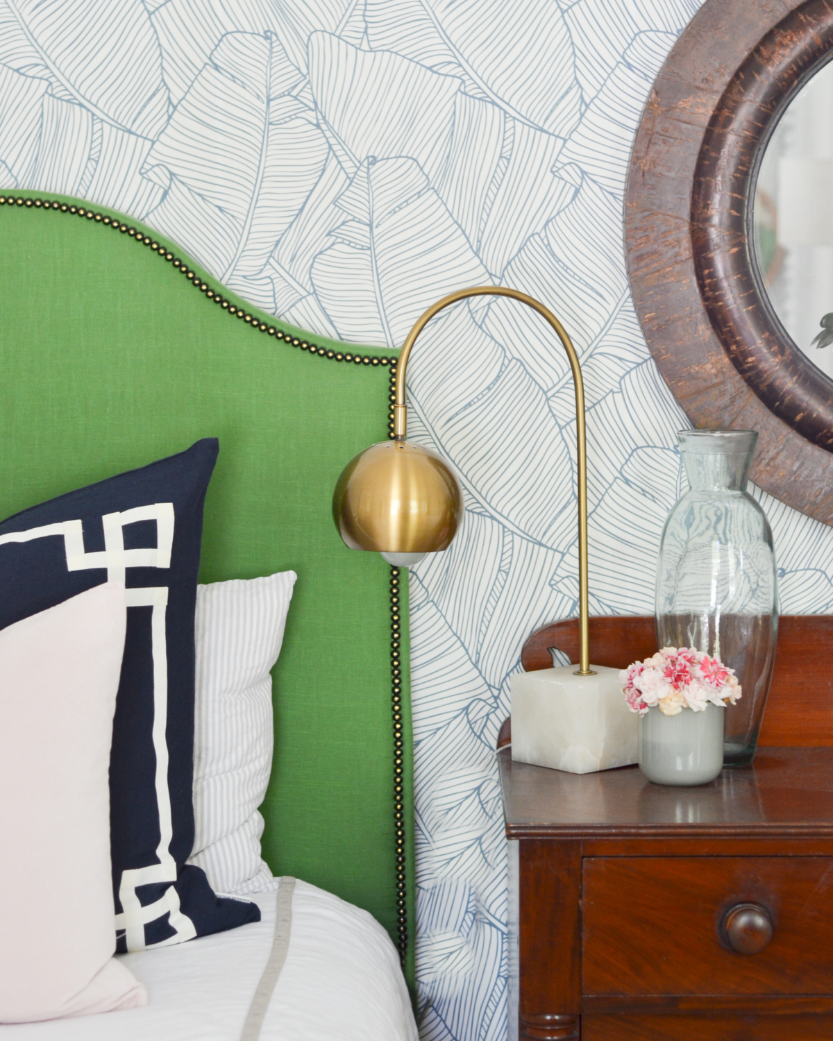 Wallpapered bedroom with twin beds, green upholstered headboards, navy blue, brass, and coral accents