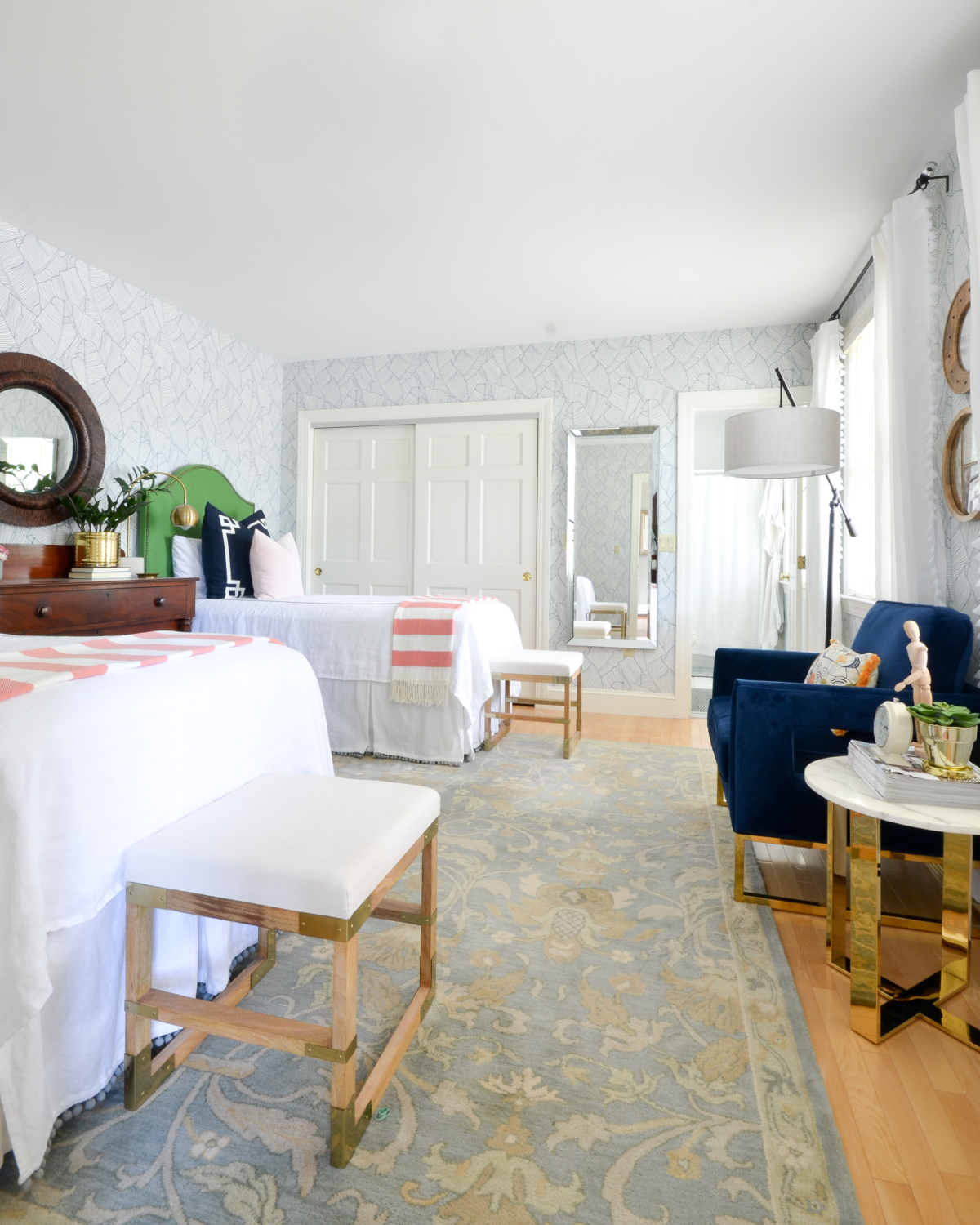 Wallpapered bedroom with twin beds, green upholstered headboards, navy blue, brass, and coral accents