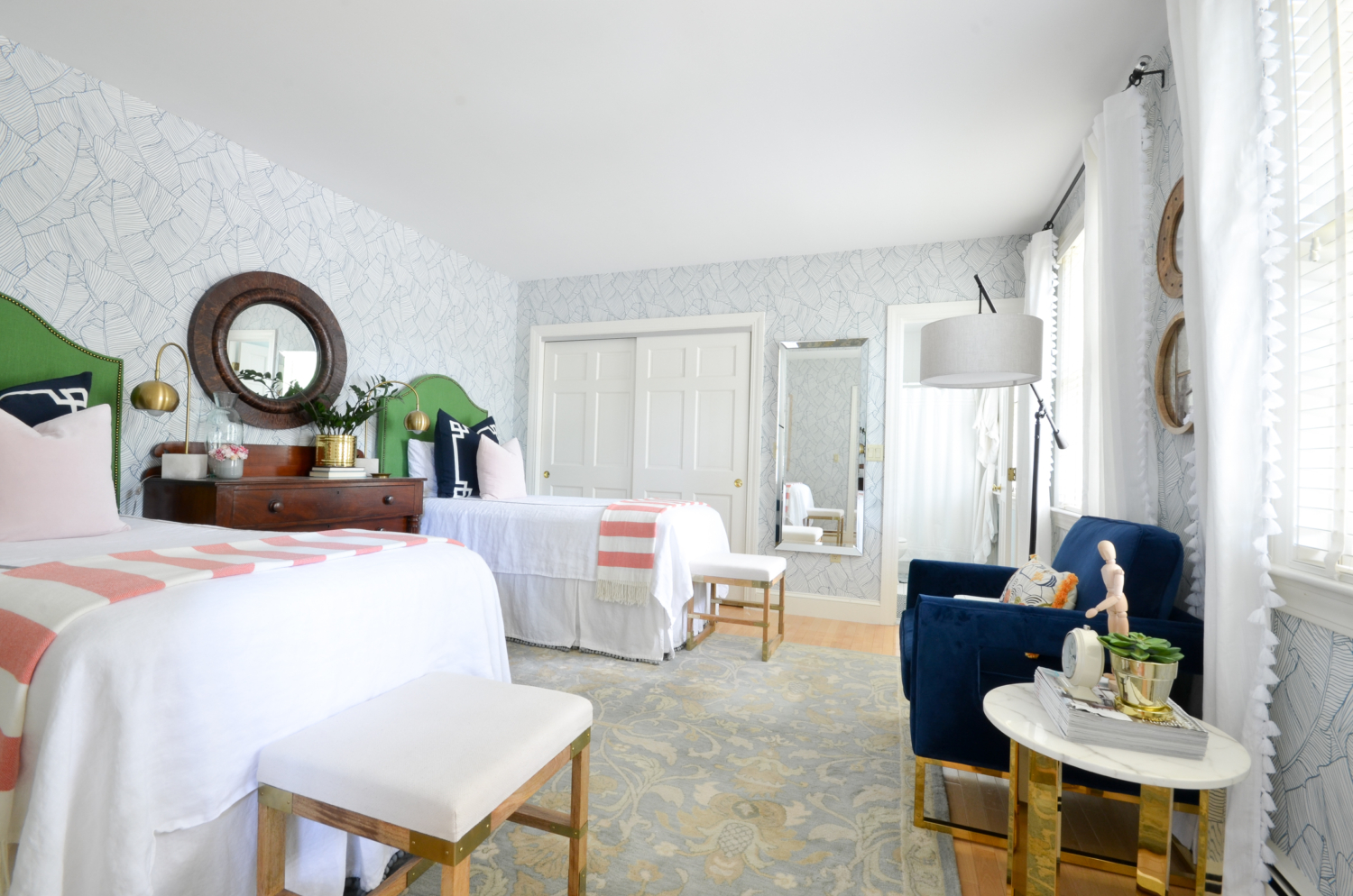 Wallpapered bedroom with twin beds, green upholstered headboards, navy blue, brass, and coral accents