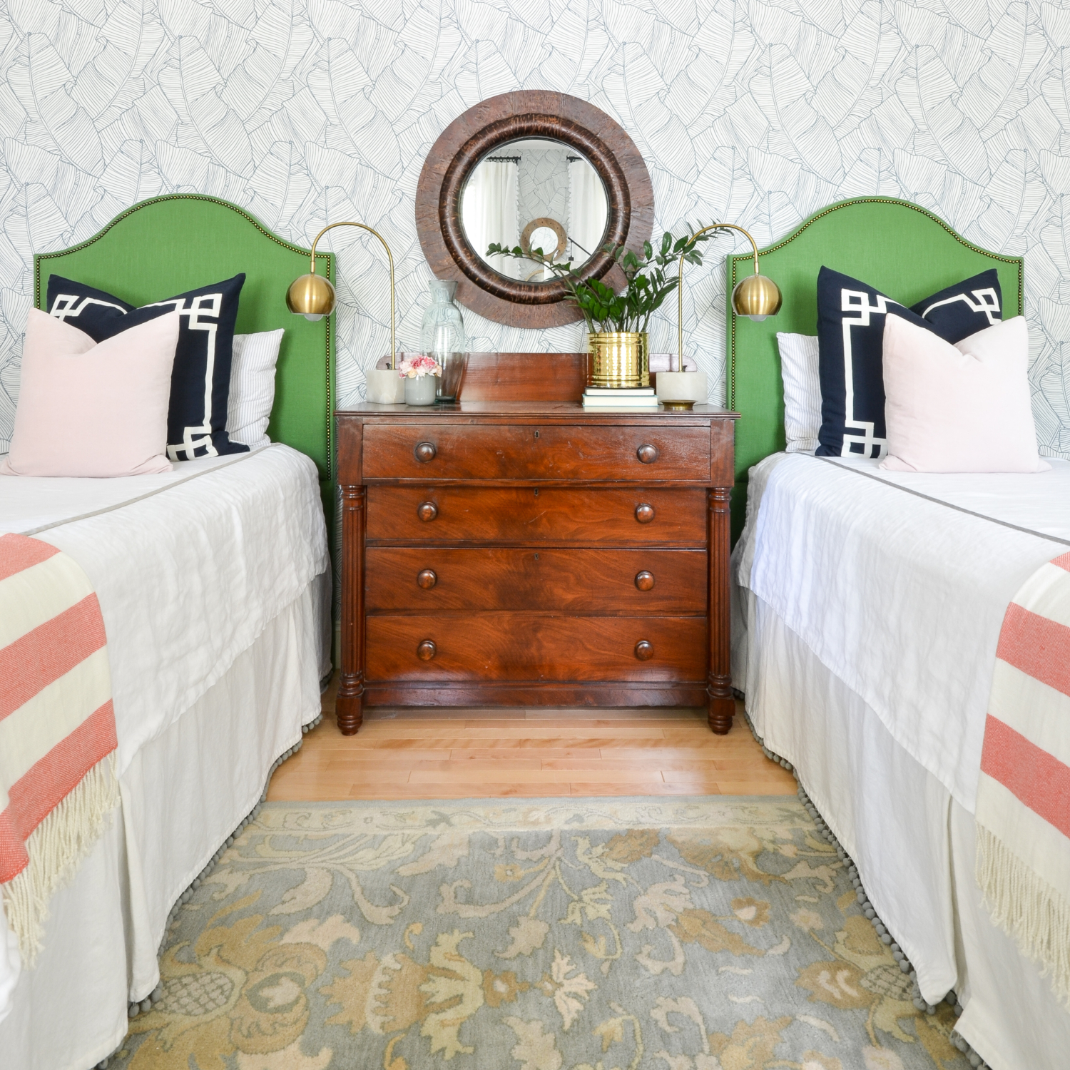 Wallpapered bedroom with twin beds, green upholstered headboards, navy blue, brass, and coral accents