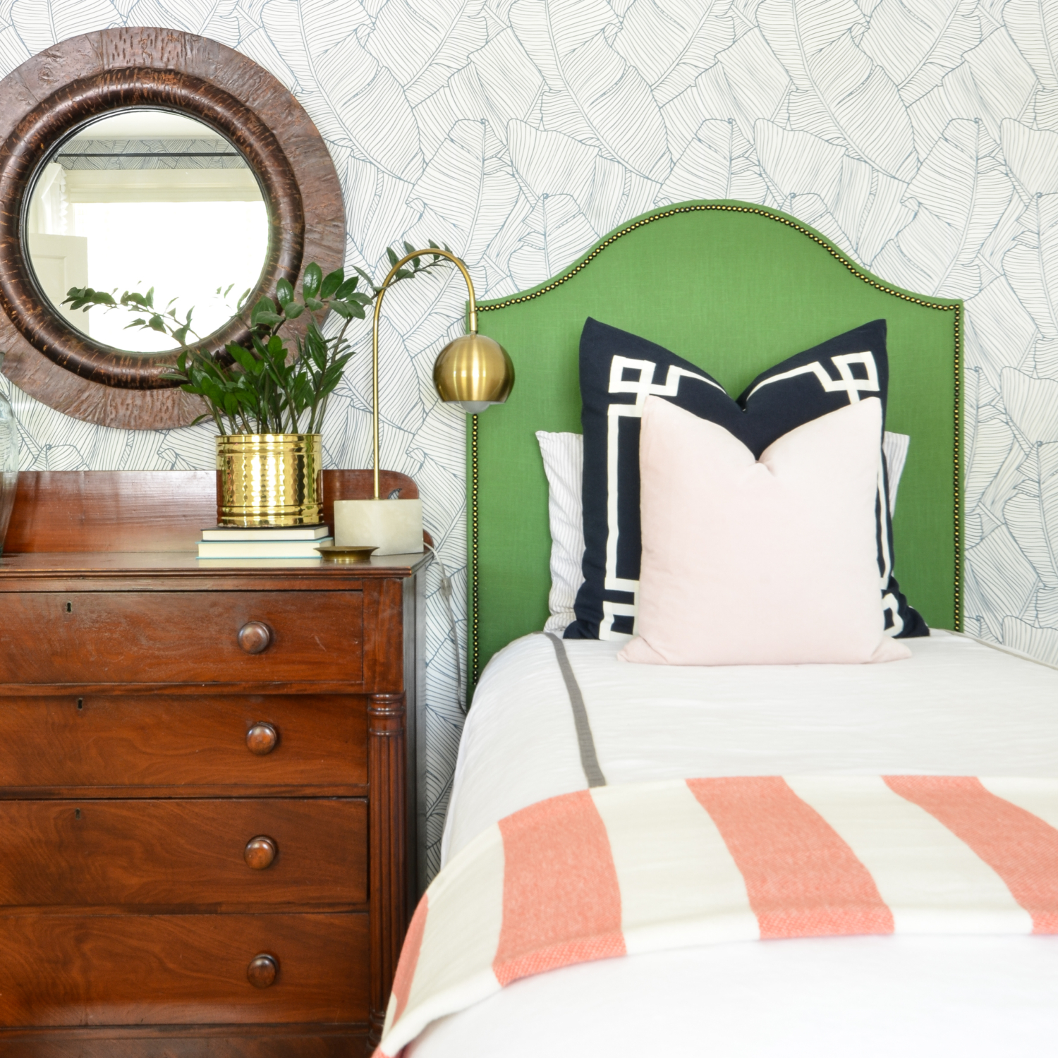 Wallpapered bedroom with twin beds, green upholstered headboards, navy blue, brass, and coral accents