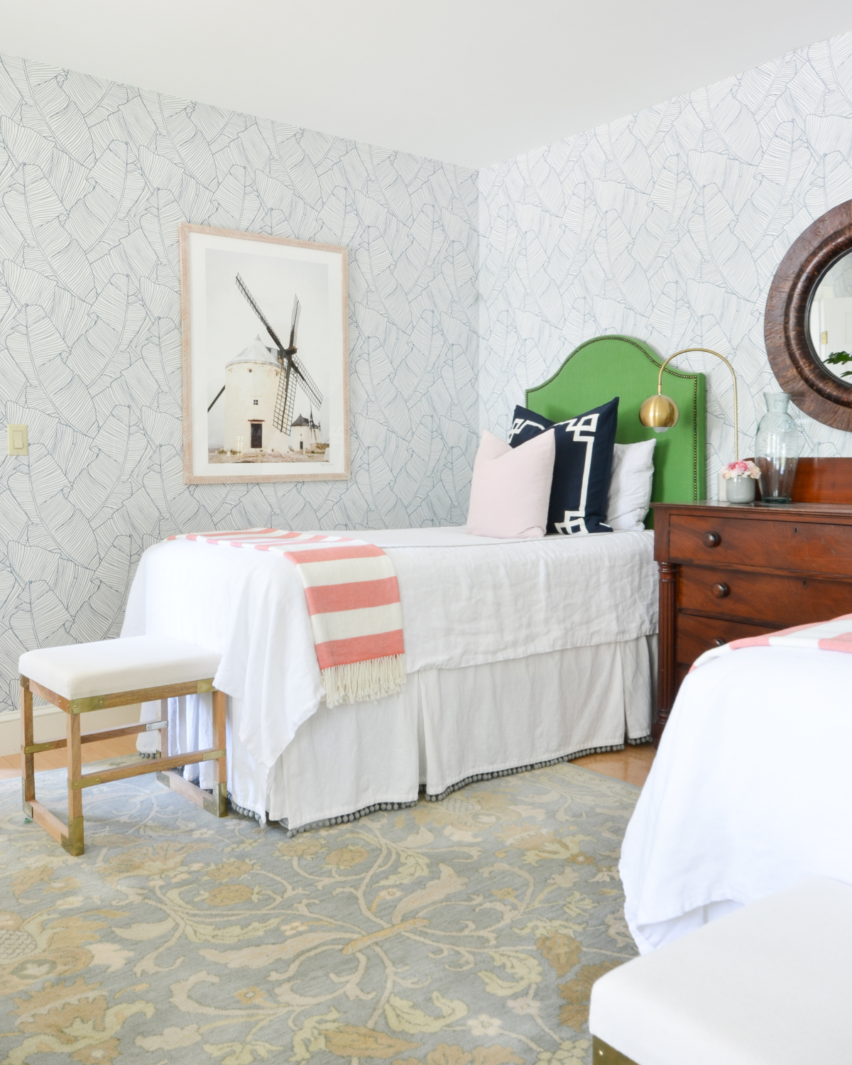 Wallpapered bedroom with twin beds, green upholstered headboards, navy blue, brass, and coral accents