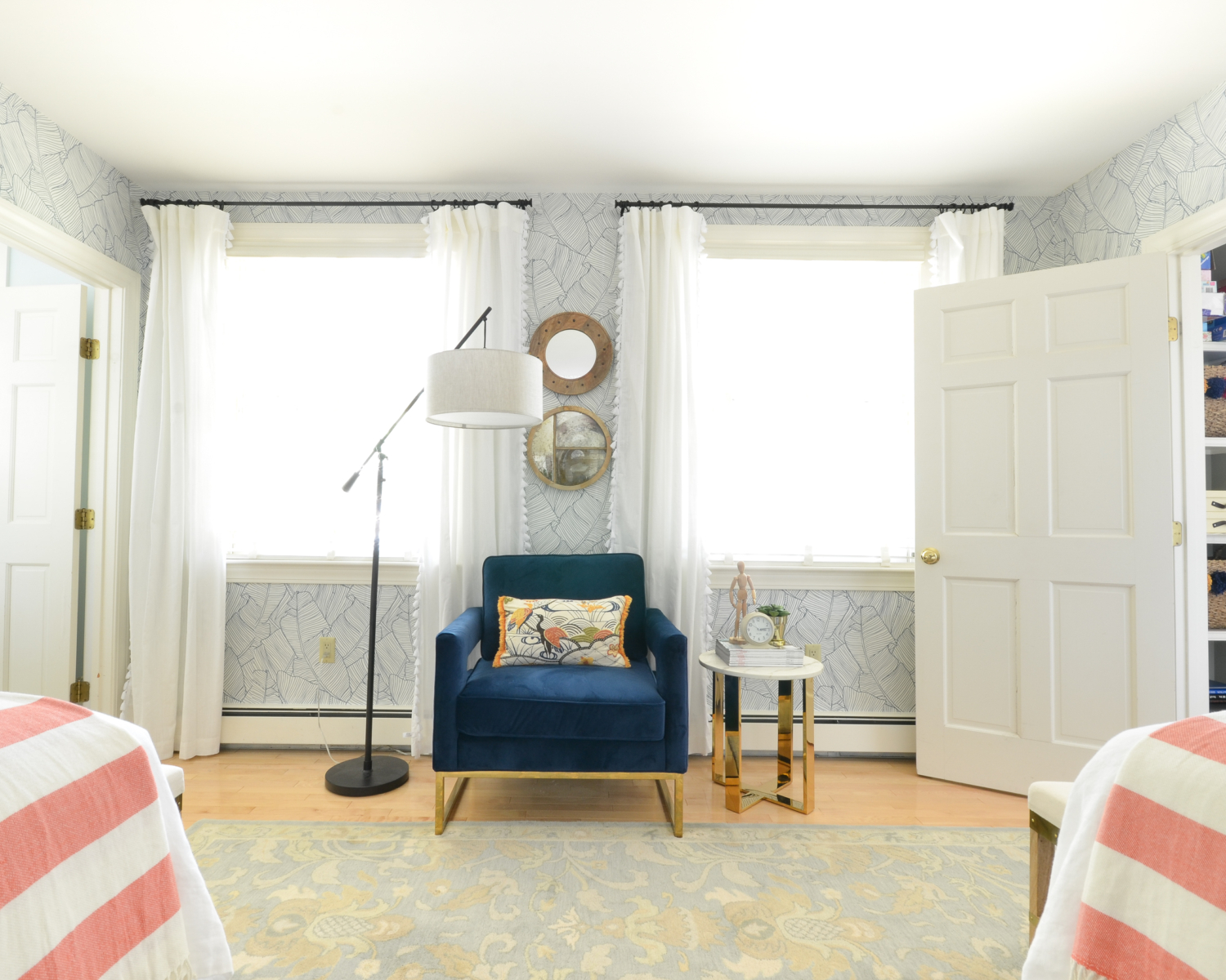 Wallpapered bedroom with twin beds, green upholstered headboards, navy blue, brass, and coral accents