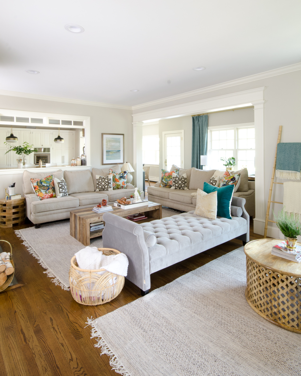 Beautiful neutral family room with pops of color and wood accents. Backless sofa divides the long room into two seating areas. Nice mix of traditional and rustic styles. Transom windows between the family room and kitchen.