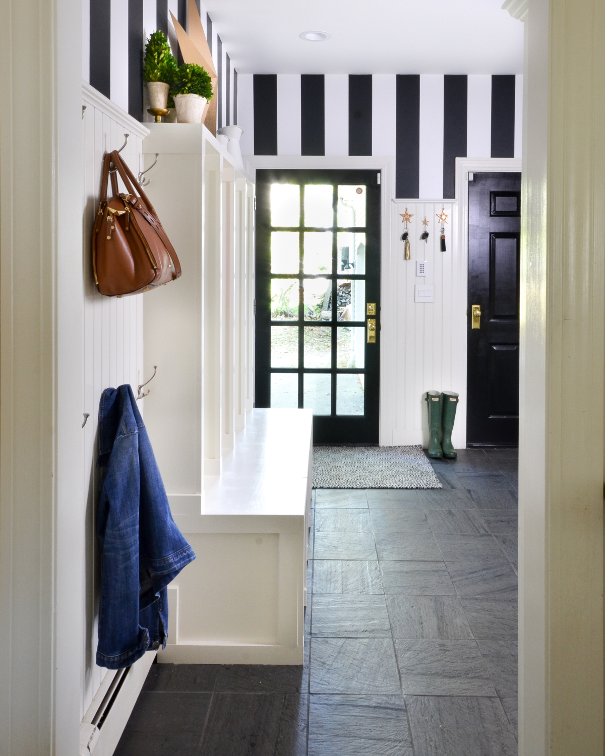 Black and white mudroom with striped wallpaper, beadboard, custom cubbies, black doors, and chunky brass doorknobs