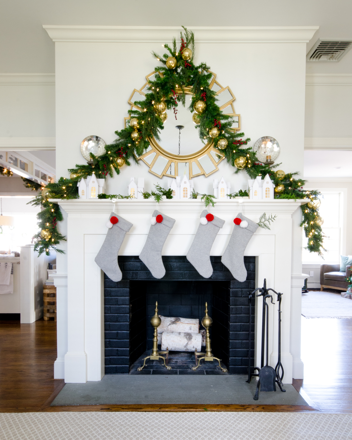 Classic Christmas mantle with lush garland, village houses, white, grey, gold, and red.