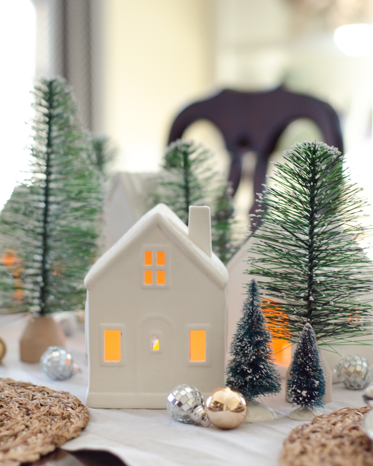 A simple and classic Christmas dining room with ceramic houses and bottle brush trees used as a Christmas centerpiece idea.