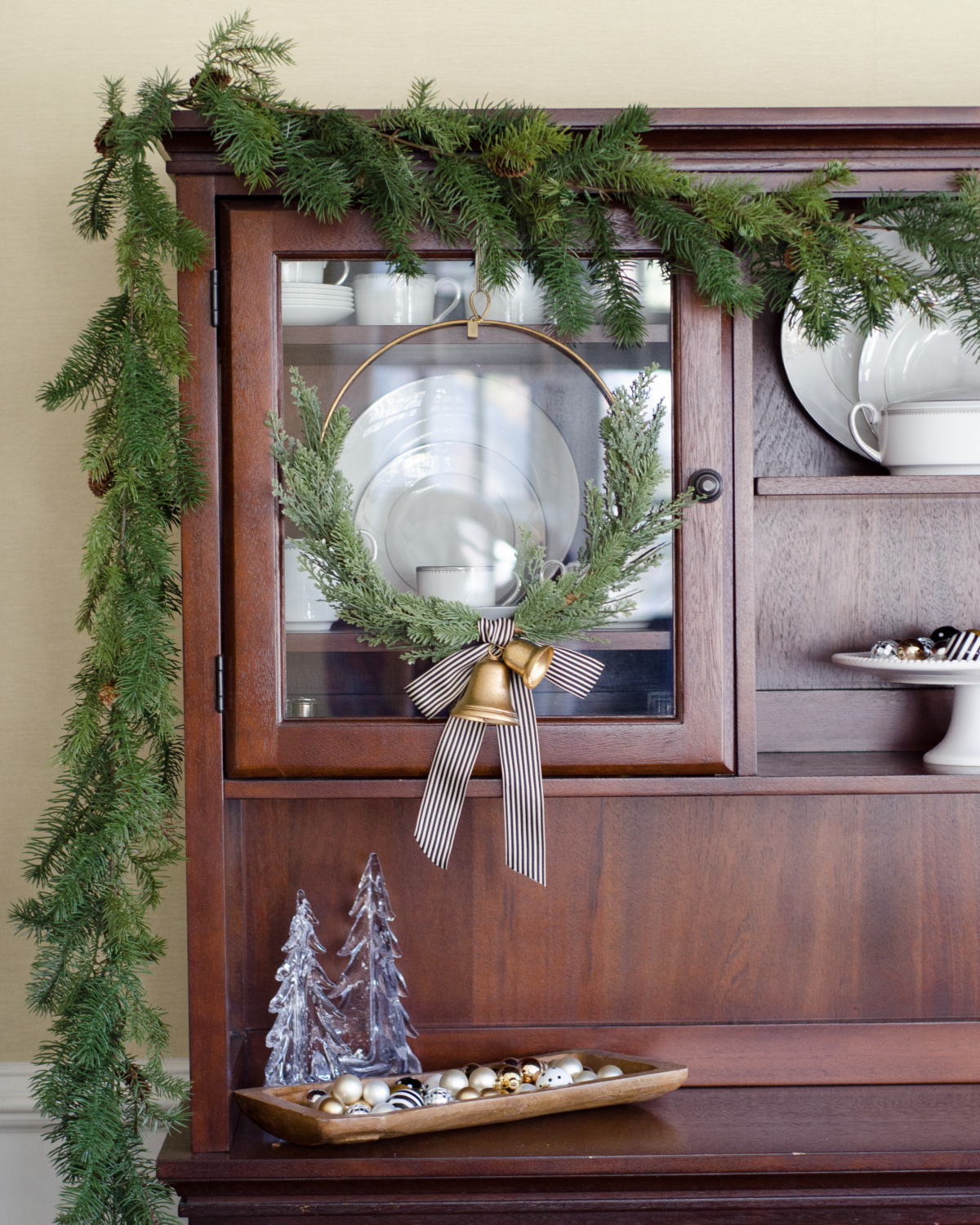 Simple greenery and gold bells on a Christmas hutch in the dining room