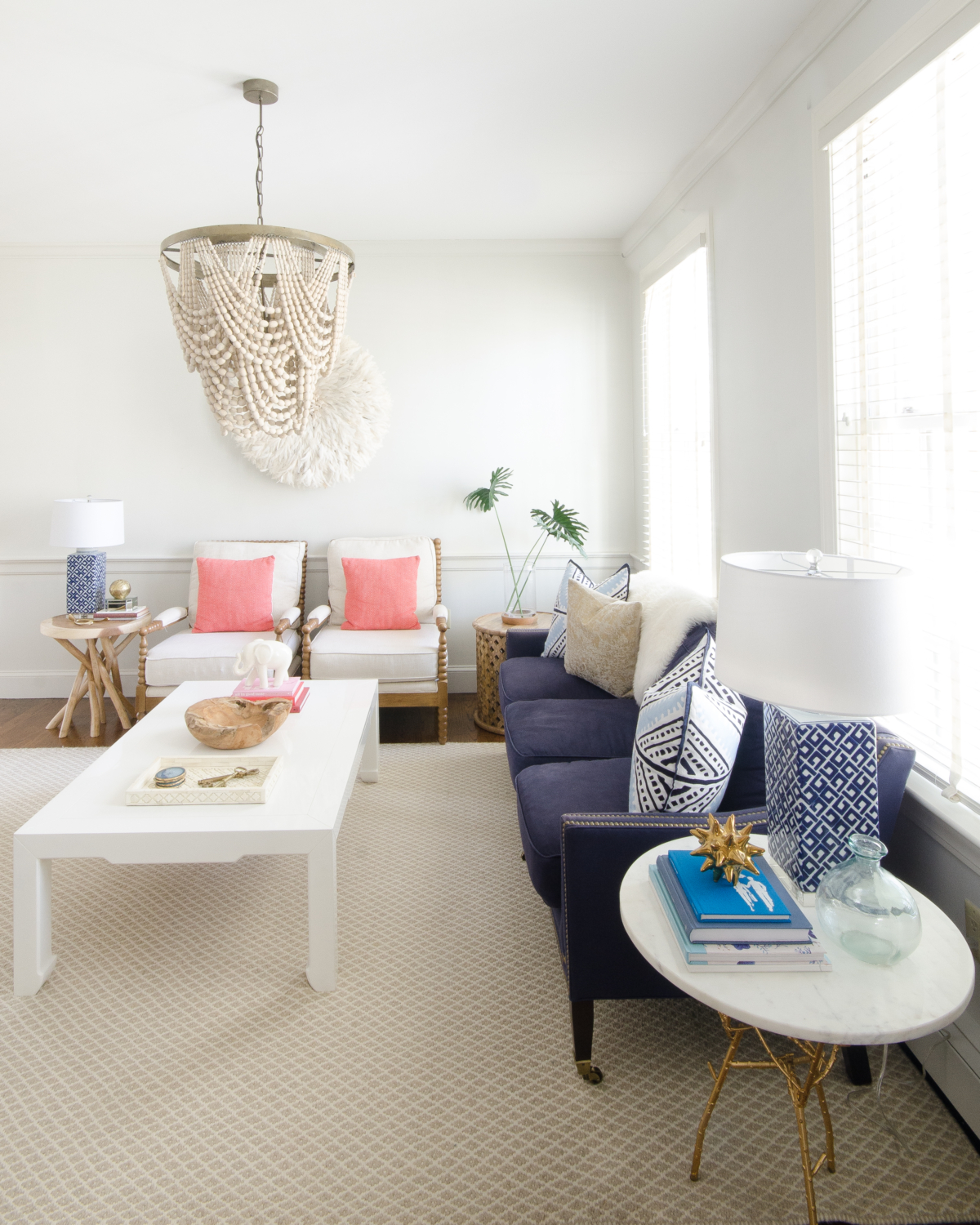 Classic living room design with a slight boho spin. A simple palette of blue, white, and coral keeps the room feeling soft and neutral with a just a bit of color. A draped beaded pendant light is the centerpiece of the room and a total showstopper.