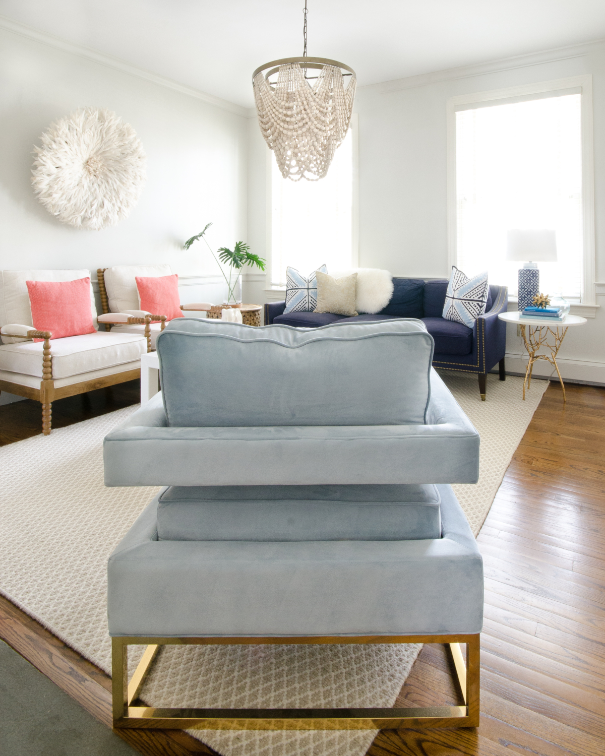 Classic living room design with a slight boho spin. A simple palette of blue, white, and coral keeps the room feeling soft and neutral with a just a bit of color. A draped beaded pendant light is the centerpiece of the room and a total showstopper.