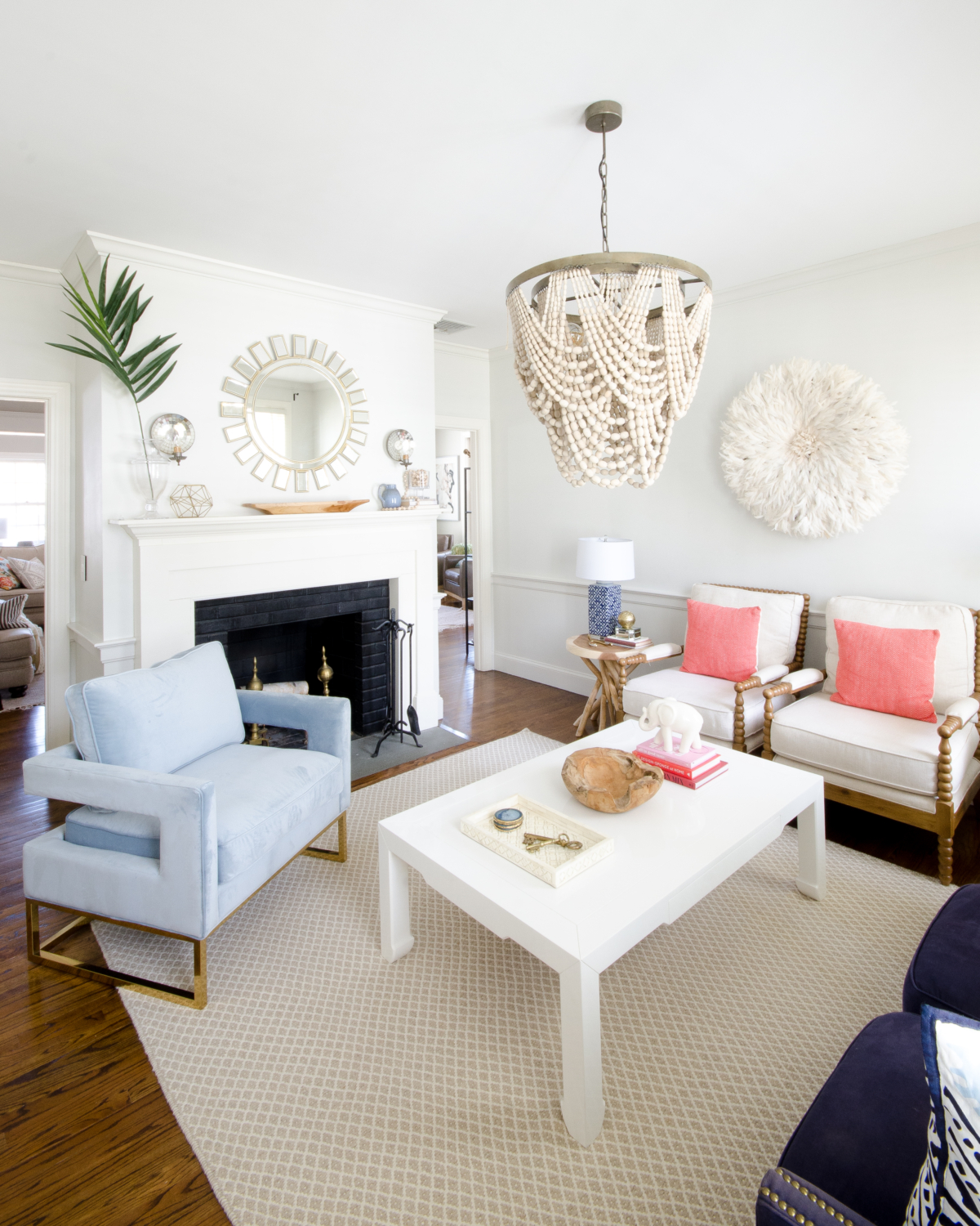 Classic living room design with a slight boho spin. A simple palette of blue, white, and coral keeps the room feeling soft and neutral with a just a bit of color. A draped beaded pendant light is the centerpiece of the room and a total showstopper.