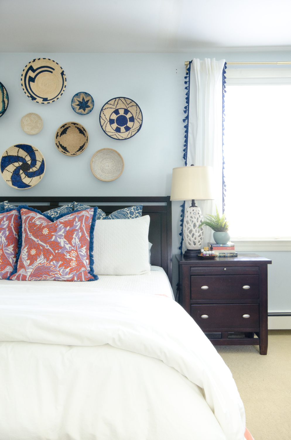 A bright, happy blue and white bedroom with pops of coral and woven basket wall art