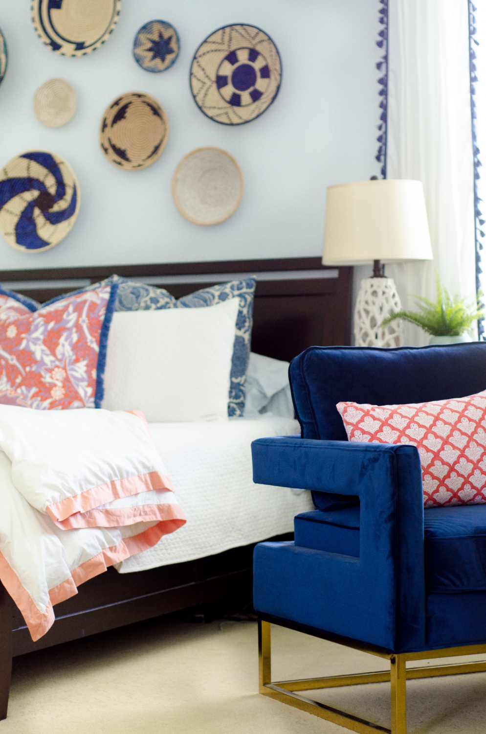 A bright, happy blue and white bedroom with pops of coral and woven basket wall art