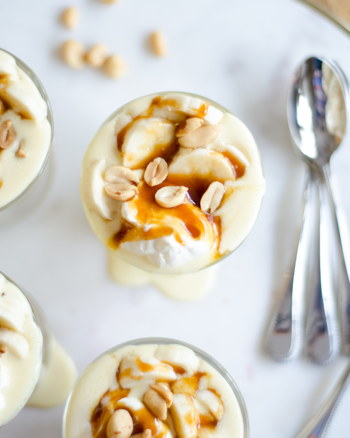 Gluten free banana cream pie recipe, in parfait form! Gorgeous individual dessert servings topped with salted caramel and peanuts for a banana cream pie like you've never tasted before!