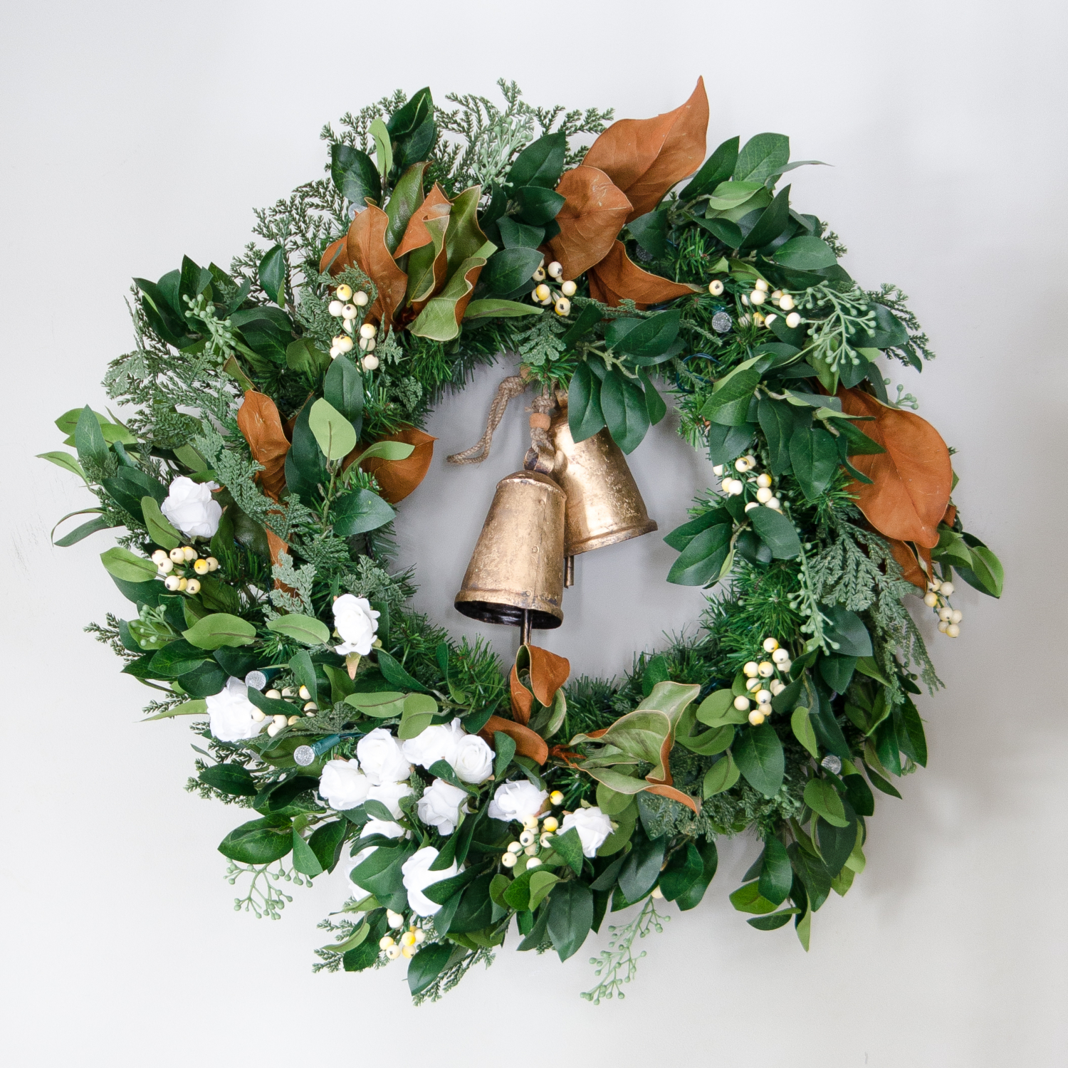 Christmas wreath with magnolia, white berries, white flowers, and gold bells