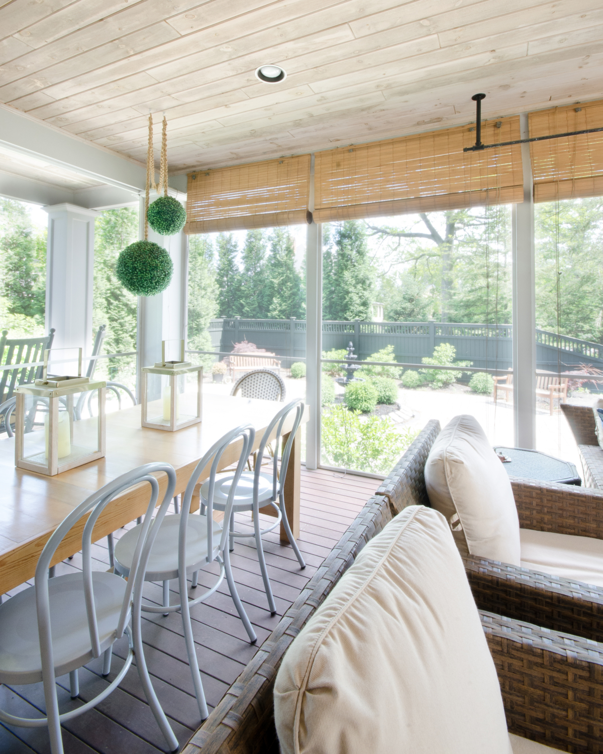 Screened porch space with dining and seating areas, a wood planked ceiling, and built in fireplace. 