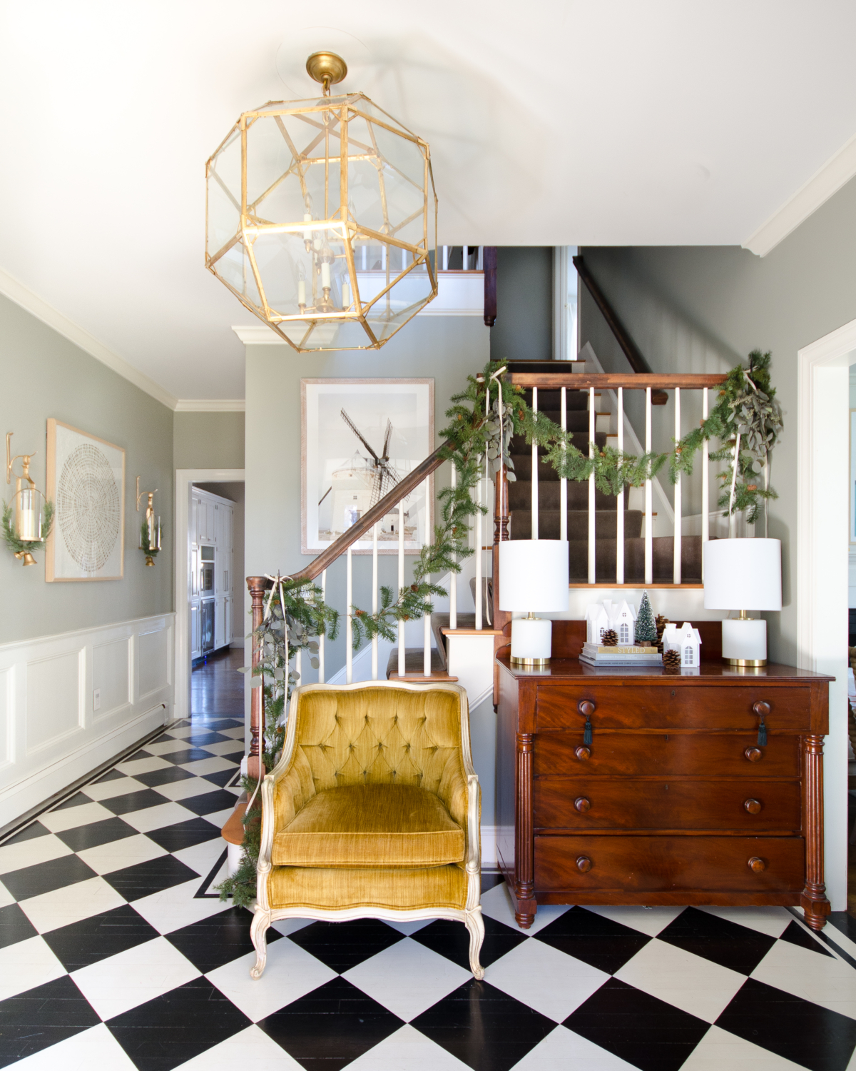 Christmas entryway with black and white checkered floors, simple evergreen and eucalyptus garland, and ivory velvet ribbon. Room features a more affordable version of the Morris Lantern.