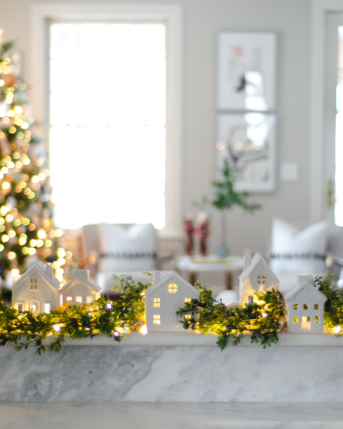 Christmas decorating ideas with white ceramic houses, boxwood garland, and twinkle lights.