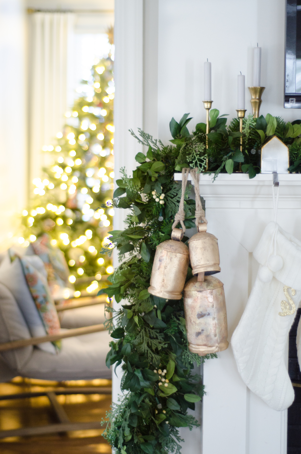 Christmas mantle with a lush garland, white cable knit stockings, gold bells, and vintage brass tulip candlesticks.