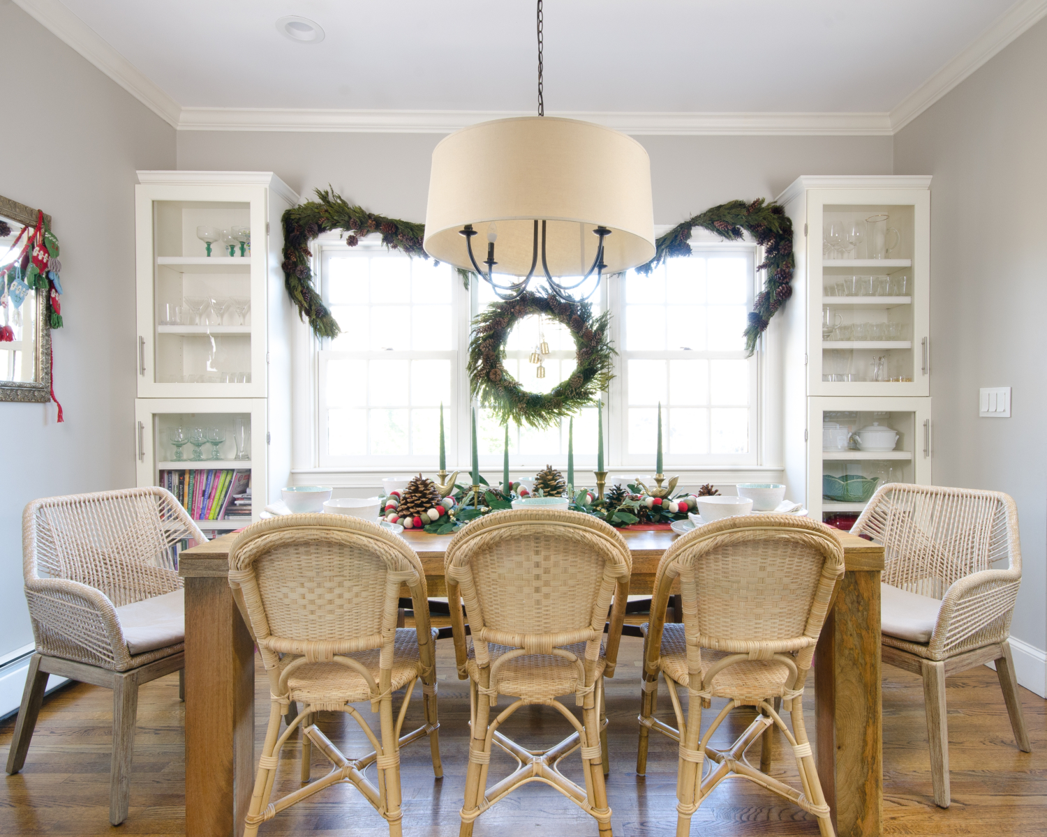 Neutral Christmas table setting in the kitchen featuring preserved cedar garland and a wreath, sunwashed Riviera side chairs, and woven rope armchairs. 