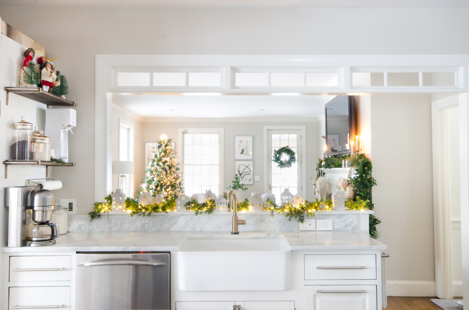 Christmas kitchen with white ceramic houses, boxwood garland, and twinkle lights.