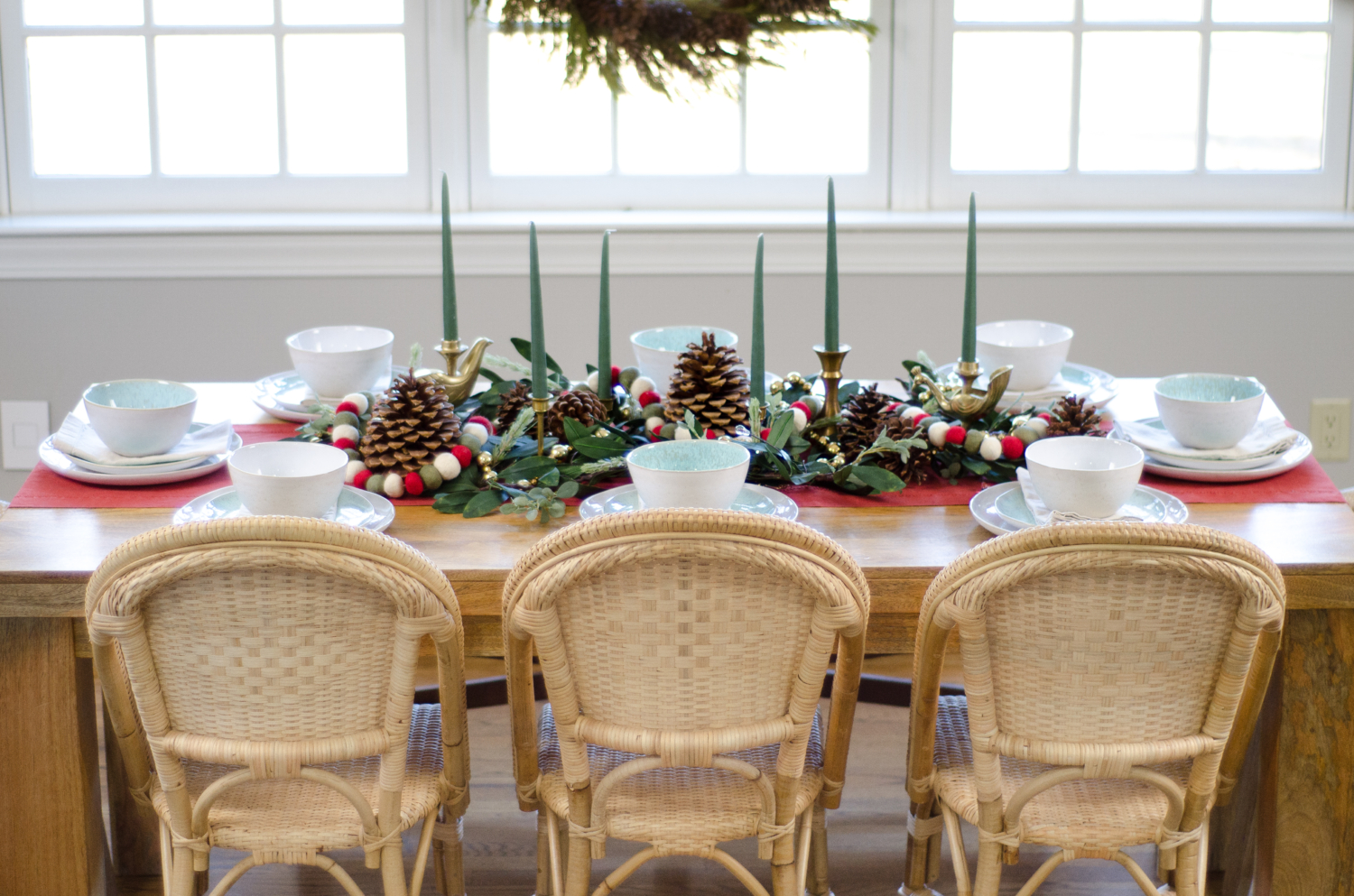 Neutral Christmas table setting in the kitchen featuring preserved cedar garland and a wreath, sunwashed Riviera side chairs, and woven rope armchairs. 