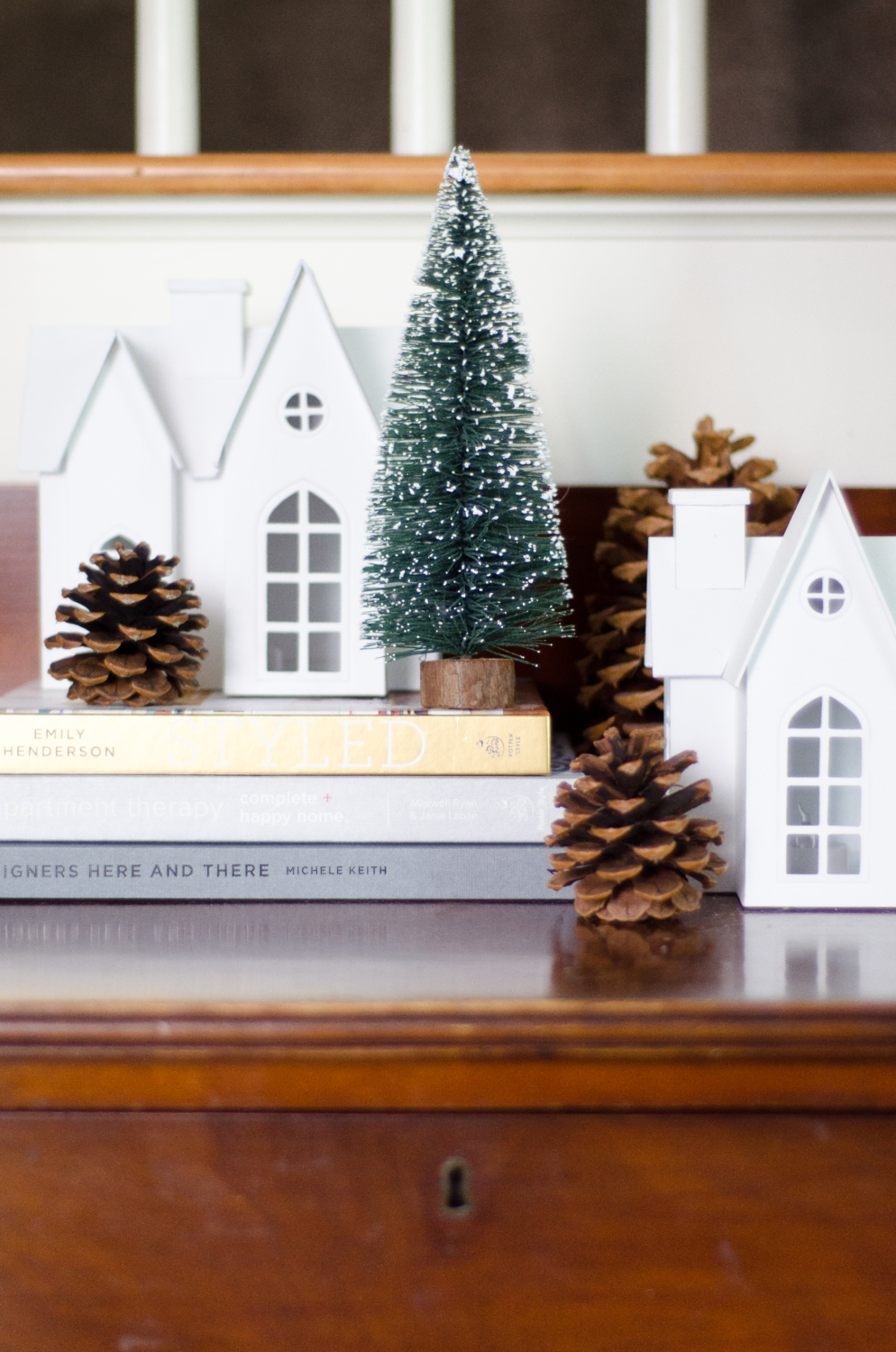 Neutral Christmas vignette with white village houses, bottle brush trees, and pinecones.