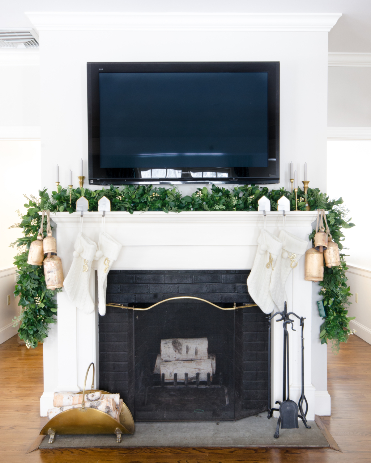 Christmas mantle with a lush garland, white cable knit stockings, gold bells, and vintage brass tulip candlesticks.